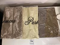 Three new pashmina scarves in beige, cream, and brown, each still in clear plastic packaging.