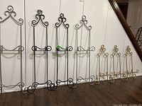 Seven metal plate racks of different sizes and three colors displayed against a white wall, showing their full height and design details.