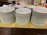 Stack of three separate piles of white porcelain plates with green stickers on some plates.