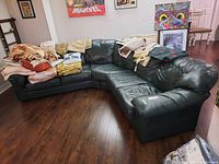 Full view of the dark green sectional leather couch with five seats, with fabric items draped on it and surrounding area.