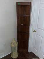Front view of laminate corner shelving unit and beige metal glass lantern positioned beside it.