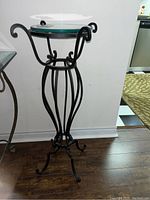 Full view of black metal stand with decorative curved legs and framework supporting a round glass top.