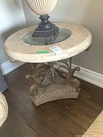 Side angle view showing the stone composite table top with glass insert and wrought metal base with carved stone composite footing beneath.