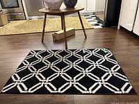 Photo of the black rectangular rug with a white geometric interlocking pattern on wood floor.