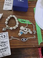 Photo showing four sterling silver bracelets including a branded Tiffany 925 bracelet with multiple round beads and charms, a chain bracelet with a blue evil eye charm, and two additional silver chain bracelets.