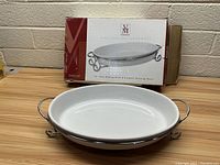 Photo of 13 inch oval white ceramic baking dish on wooden surface with metal serving rack under it and original box behind.