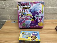 Butter Crusher Sensory Set and Tiny Tukkins Tiny Toy Playset box on wooden table against brick wall