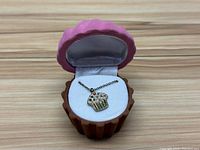 Cupcake charm necklace inside cupcake-shaped jewelry box on wooden surface.