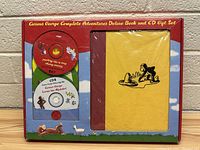 Front view of the Curious George Complete Adventures Deluxe Book and CD Gift Set showing the yellow hardcover book and four CDs inside the box.