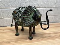 Side view of metal elephant sculpture showing details of ears, tail with curled end, and body adorned with glass gems.