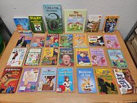 Full view of the large lot of kids books laid out on a table showing assorted titles and colorful covers