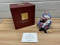 Photo showing the porcelain Santa Claus figure holding a child with a dog beside, next to the original red Lenox box and certificate of authenticity.