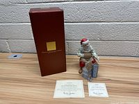 Photo of Lenox porcelain Santa figure painting dollhouse with original red box and two certificates on table.