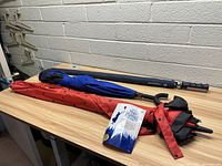 Lot of 3 umbrellas: one rolled in a navy blue sleeve, one with a blue and black canopy and another with red and black polka dots on the canopy and sleeve.