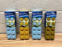 Four LEGO Chima pencil cases in original packaging, two light blue and two yellow, displayed upright against textured wall.