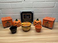 View of the lot showing seven ceramic items and one picture frame, including two large orange jack o lanterns in original boxes, three differently styled ceramic bowls, and one Halloween picture frame