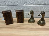 Wooden and brass bird-themed bookends resting on wooden surface in front of brick wall.
