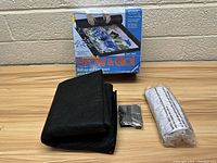 The puzzle saver mat, rubber straps, storage tube, and original box shown together on a table against a brick wall.