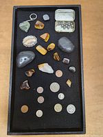 Full view of the tray showing assorted polished rocks, raw stone, keychain, small tin box of metal balls, and coins.