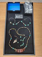 Top view of tray containing necklaces, pendants, earrings, and jewelry box with rings arranged on black fabric.