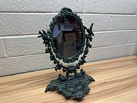 Angled view of the vintage metal mirror with ornate frame and ring holder at base showing detailed craftsmanship and patina.