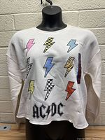 Front view of white women’s sweater with colorful lightning bolts and AC/DC logo on mannequin.