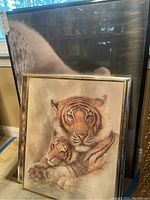 Framed print featuring a tiger with a cub, soft beige and orange tones, enclosed in a thin gold-colored frame.