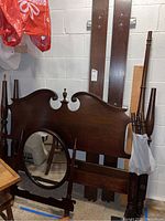 Photo showing the disassembled full size wood headboard, footboard, side rails, and oval mirror stored together in basement space.