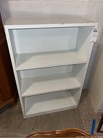 Front view of the white wooden bookcase showing three shelves and wear on the paint.