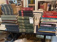 Wide view of book stacks on table including encyclopedias, novels, dictionaries, and a white typewriter.