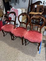 Photo showing three matching wooden dining chairs with carved accents on the upper back and red upholstered seats, placed on floor in basement setting.