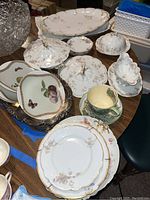 Multiple Haviland China serving pieces with floral motifs and gold trim displayed on a round wooden table, including platters, covered dishes, and a cup and saucer.