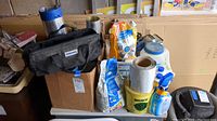 Photo of boxed and packed items on a table including grout bags, grout sealer bottles, Bissell carpet cleaner, and rolls of metal sheeting