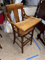 Wooden high chair angled view showing seat, tray, backrest and arm supports.