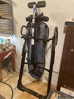 Side view of inversion table showing perforated backrest, padded headrest and attached safety straps, standing upright in basement area.