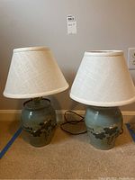 Pair of matching ceramic table lamps with floral decoration and fabric shades on floor against wall