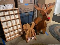 Wooden bunny and reindeer magazine racks with the wall-mount shadowbox beside them on floor by shelving unit.