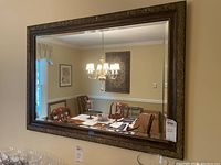 Front view of the large rectangular mirror hung on wall, showing its ornate dark brown carved frame and clear reflection of dining room interior.
