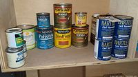 Wide shot showing all cans in the lot arranged on a shelf, including multiple Minwax and Bartley product cans.