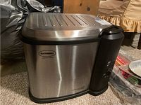 Electric turkey fryer by Buttermail, stainless steel body with black control panel and lid, placed on carpeted floor.