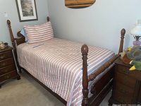 Full view of the wooden twin bed frame made with carved posts, set up with red and white striped linens including pillow and sheet.