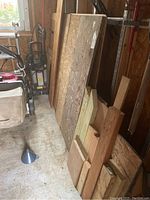 Large plywood and oriented strand board leaning against wall with smaller wood pieces in front.