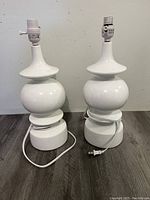 Two white modern table lamps without shades, cords visible, showing full lamp shape and style.