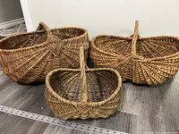 Three large antique wicker baskets with handles arranged on floor, showing star design woven detail on the handles.