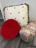 Full view of all three pillows showing cream square pillow with bee embroidery, red round velvet pillow, and blush pleated satin bolster pillow