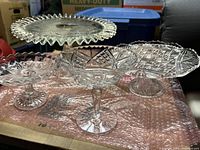 Four vintage clear cut glass cake stands and candy dish displayed together showing intricate patterns and pedestal stems.