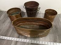 Photo showing all four vintage copper and brass planters together on a wooden floor with a measuring tape in front showing lengths.