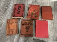 Six antique hard cover books laid on floor showing cover designs and titles, featuring art deco styles