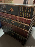 Close side and front view of the chest showing stacked book spine drawer design and round knobs.