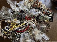 Overview of lot showing assorted colorful beaded jewelry, metal chains and plastic bags with smaller items